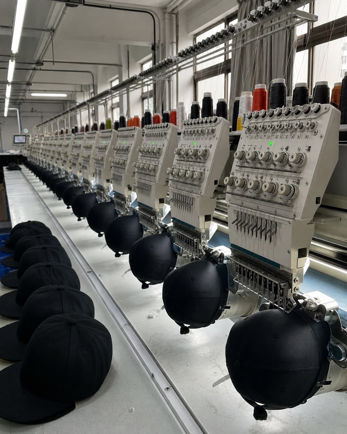 a row of multi-head embroidery machines with black caps mounted on the frames